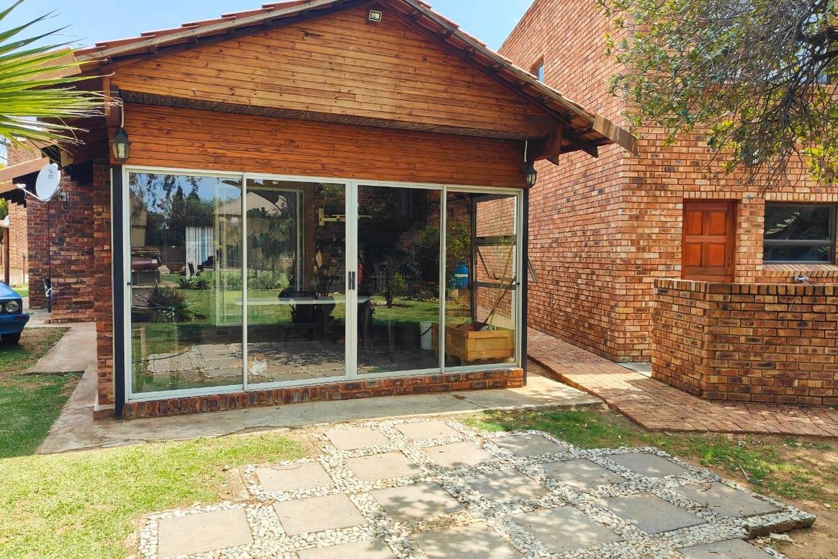Rear view of the property featuring a timber-clad structure with large sliding glass doors, adjacent to a brick building and a paved garden patio.
