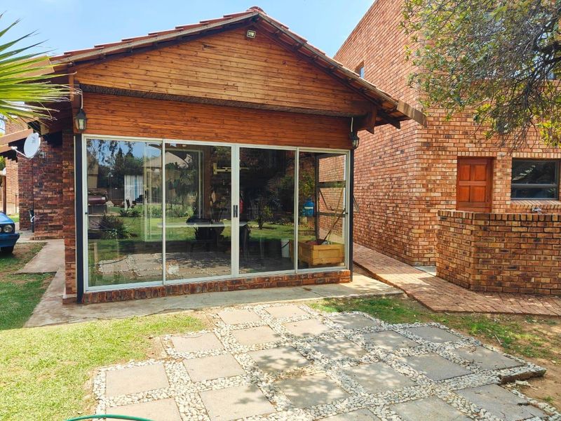 Rear view of the property featuring a timber-clad structure with large sliding glass doors, adjacent to a brick building and a paved garden patio.