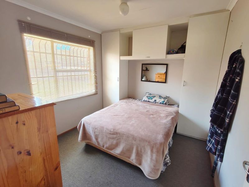 A functional bedroom featuring built-in cupboards with overhead storage, carpeted flooring, and a window fitted with venetian blinds.