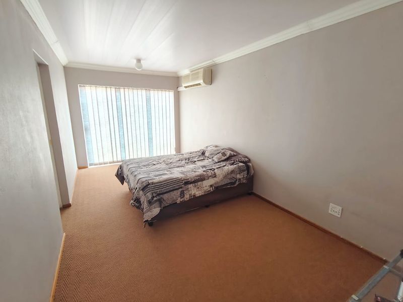 A bedroom featuring carpet flooring, vertical blinds, and a wall-mounted air conditioning unit, offering a functional space with potential for cosmetic updates.