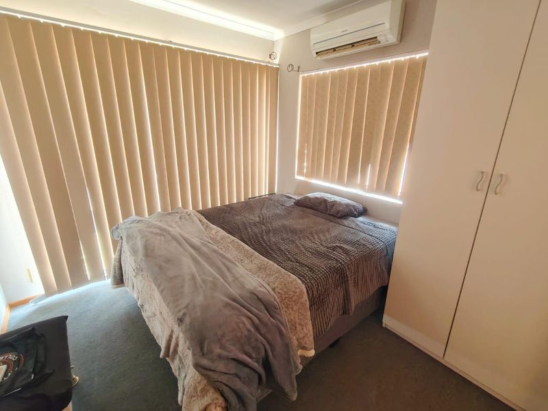 A functional bedroom featuring built-in wardrobe storage, carpeted flooring, and a wall-mounted split-system air conditioning unit for climate control.