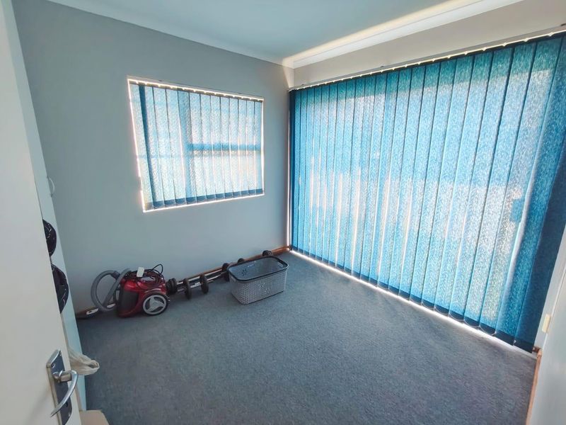 A clean, empty bedroom featuring neutral wall paint, carpeted flooring, and floor-to-ceiling vertical blinds providing ample natural light.