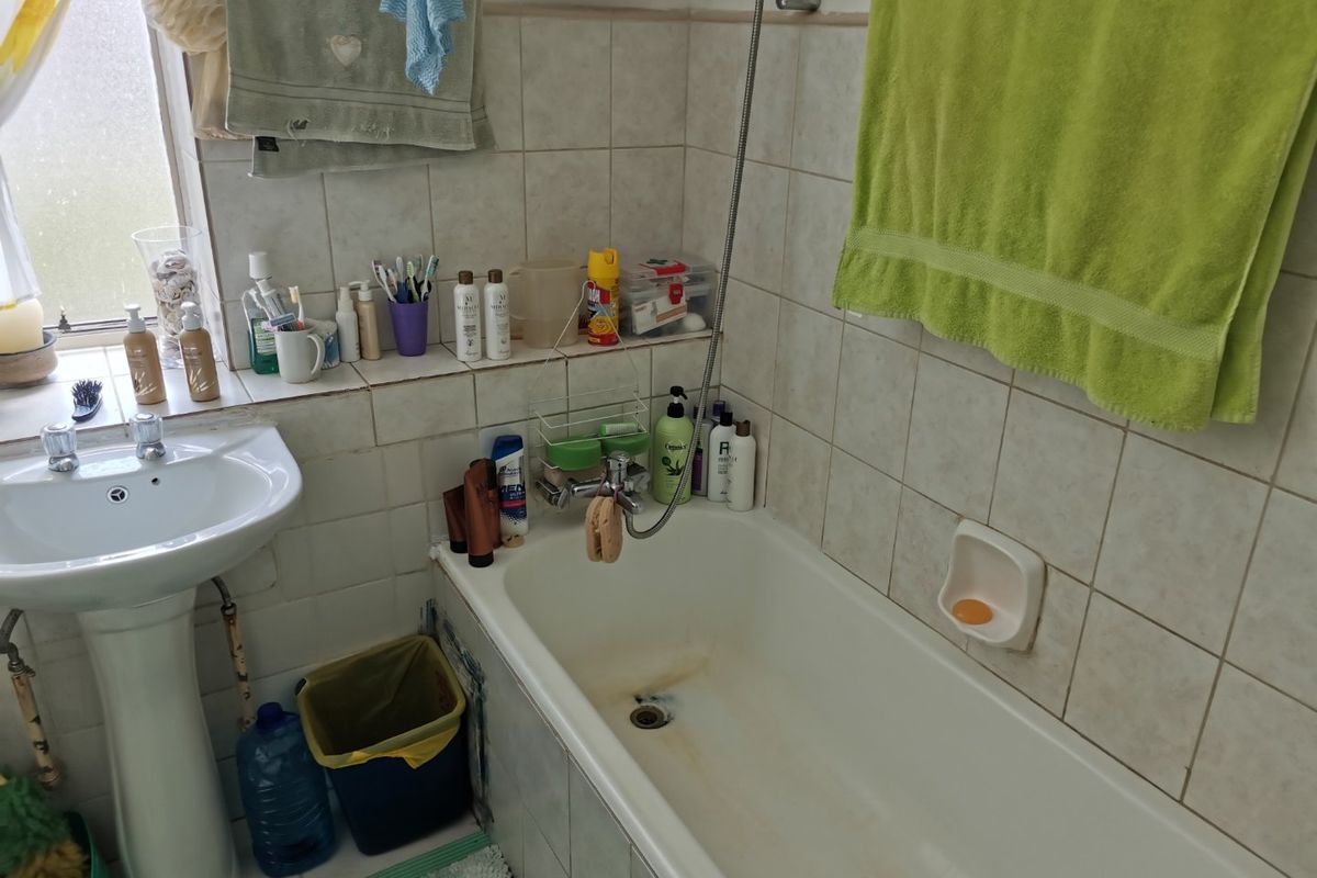 A functional bathroom featuring a pedestal washbasin and a bathtub with integrated shower mixer, finished with ceramic wall tiling.