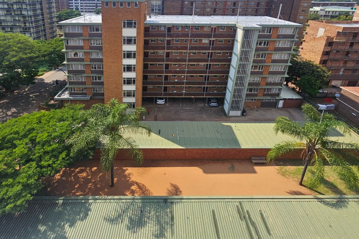 Aerial view of a multi-story commercial or residential brick building featuring a central stairwell, covered parking area, and surrounding landscaped grounds.