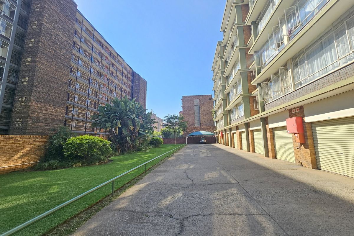 Exterior view of a commercial apartment complex featuring a paved driveway, row of garage units, and a well-maintained lawn area.
