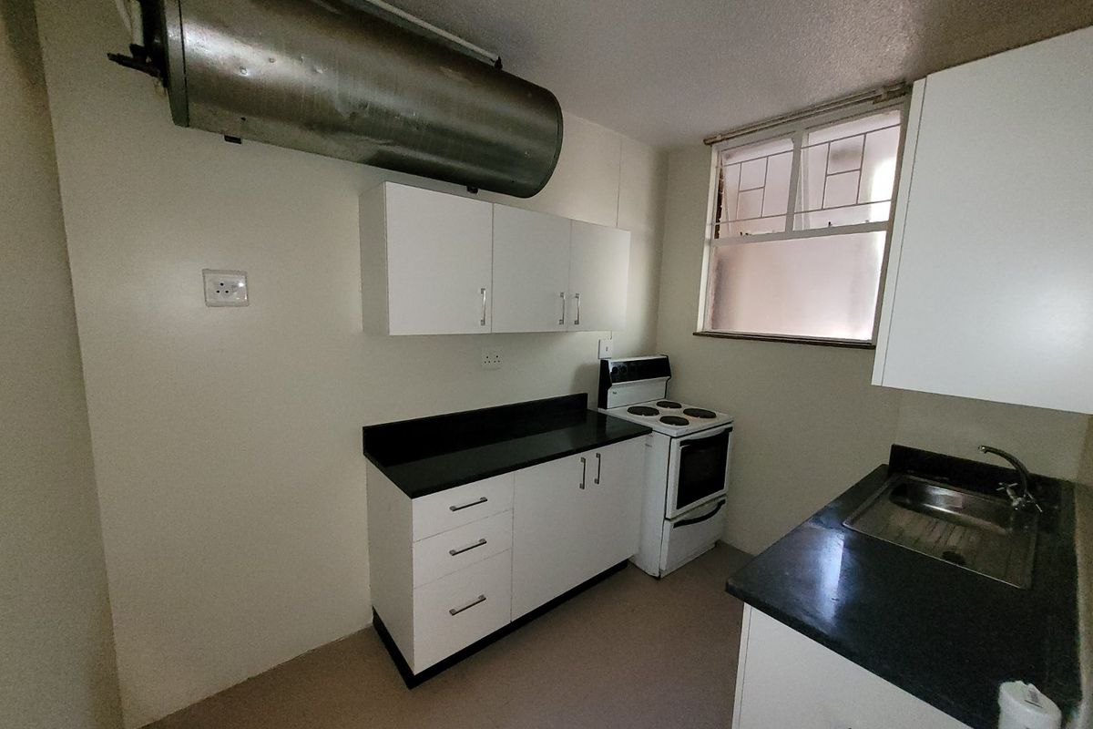 A functional kitchen featuring white cabinetry, dark countertops, a stainless steel sink, and a freestanding stove, with an exposed electric water heater.