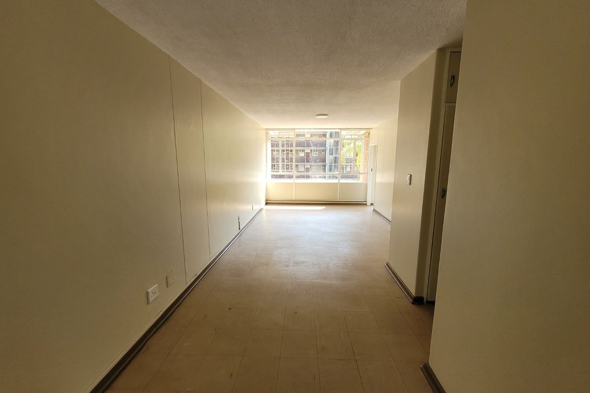 An empty, open-plan living area featuring tiled flooring, built-in storage cupboards, and a large window providing natural light.
