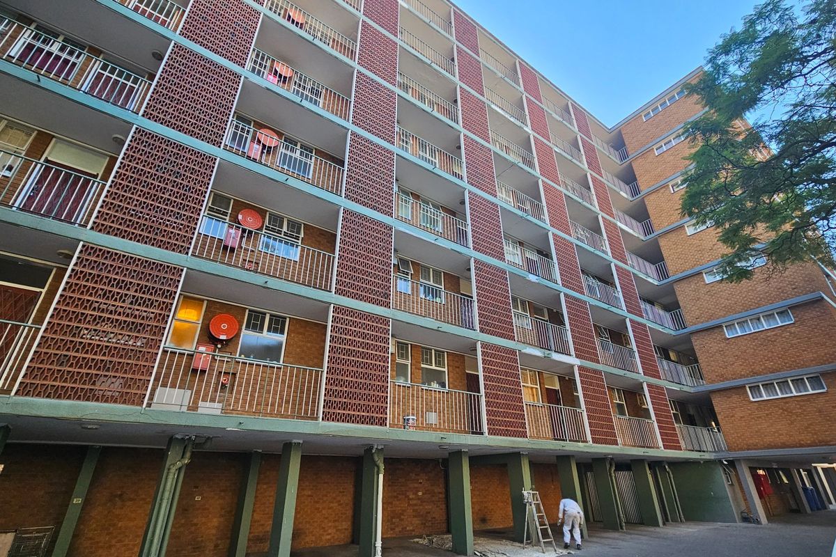 Exterior view of a multi-story commercial or residential building featuring brick facade, decorative breeze block screens, and open balcony walkways.