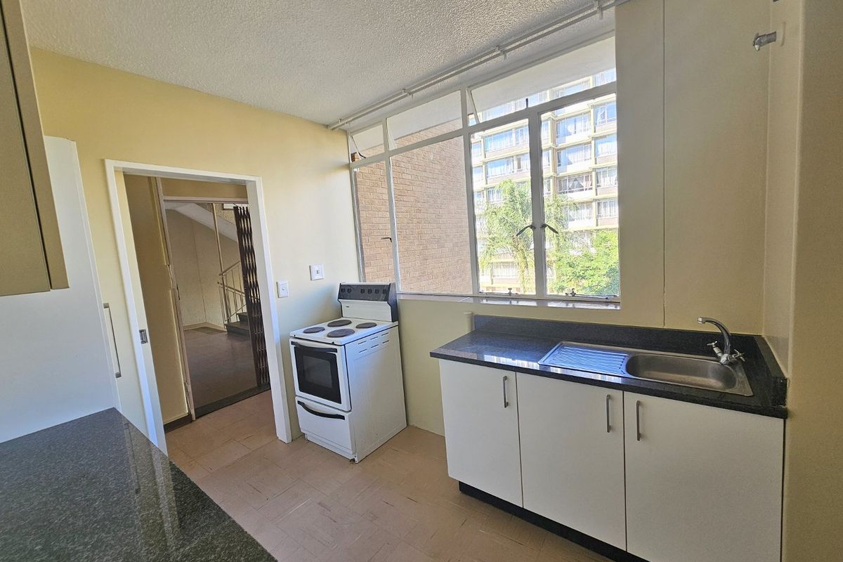 A functional kitchen featuring a freestanding electric stove, stainless steel sink, and ample cabinetry, offering a blank canvas for modern updates.
