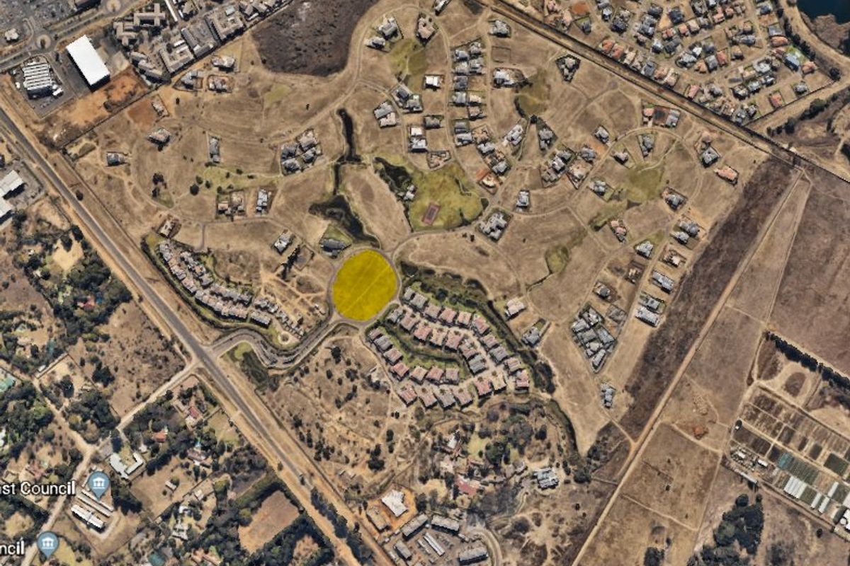 An aerial view of a residential estate development showing the layout of plots, roads, and surrounding infrastructure.