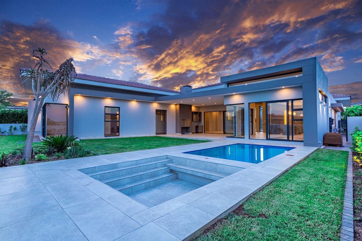 Modern rear exterior featuring a swimming pool, sunken seating area, covered patio with built-in braai, and expansive glass sliding doors.