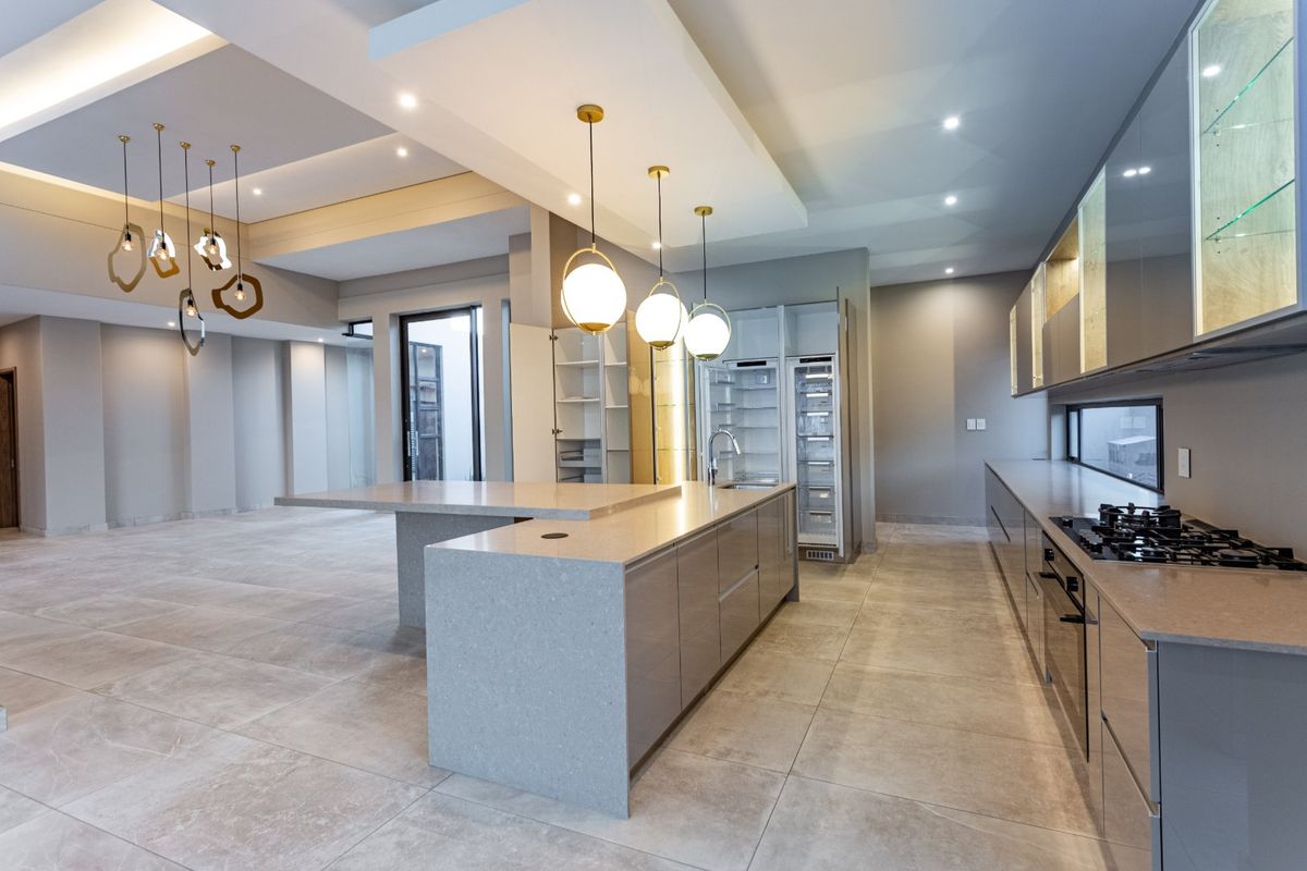 Modern, spacious kitchen featuring a large island with stone countertops, integrated appliances, sleek cabinetry, and contemporary pendant lighting in an open-plan layout.