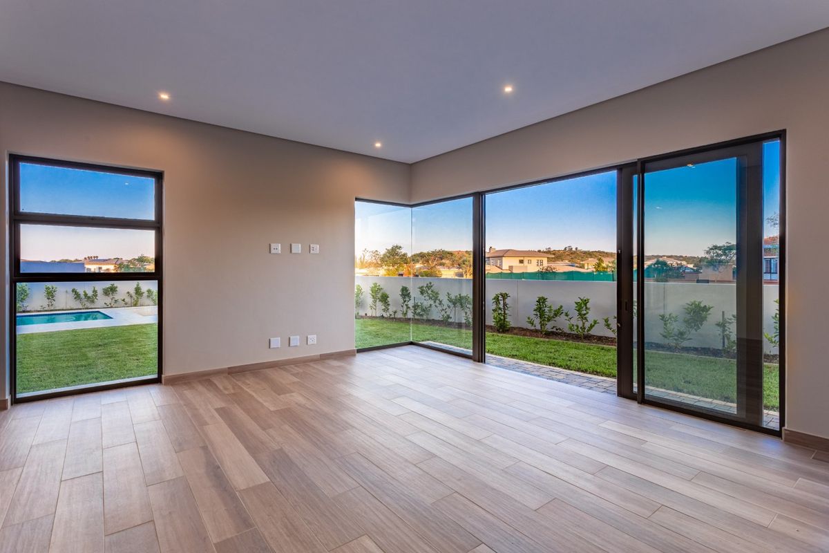 A bright, modern, and empty living room featuring large sliding glass doors, corner windows, and high-quality wood-look tile flooring with a view of the garden.