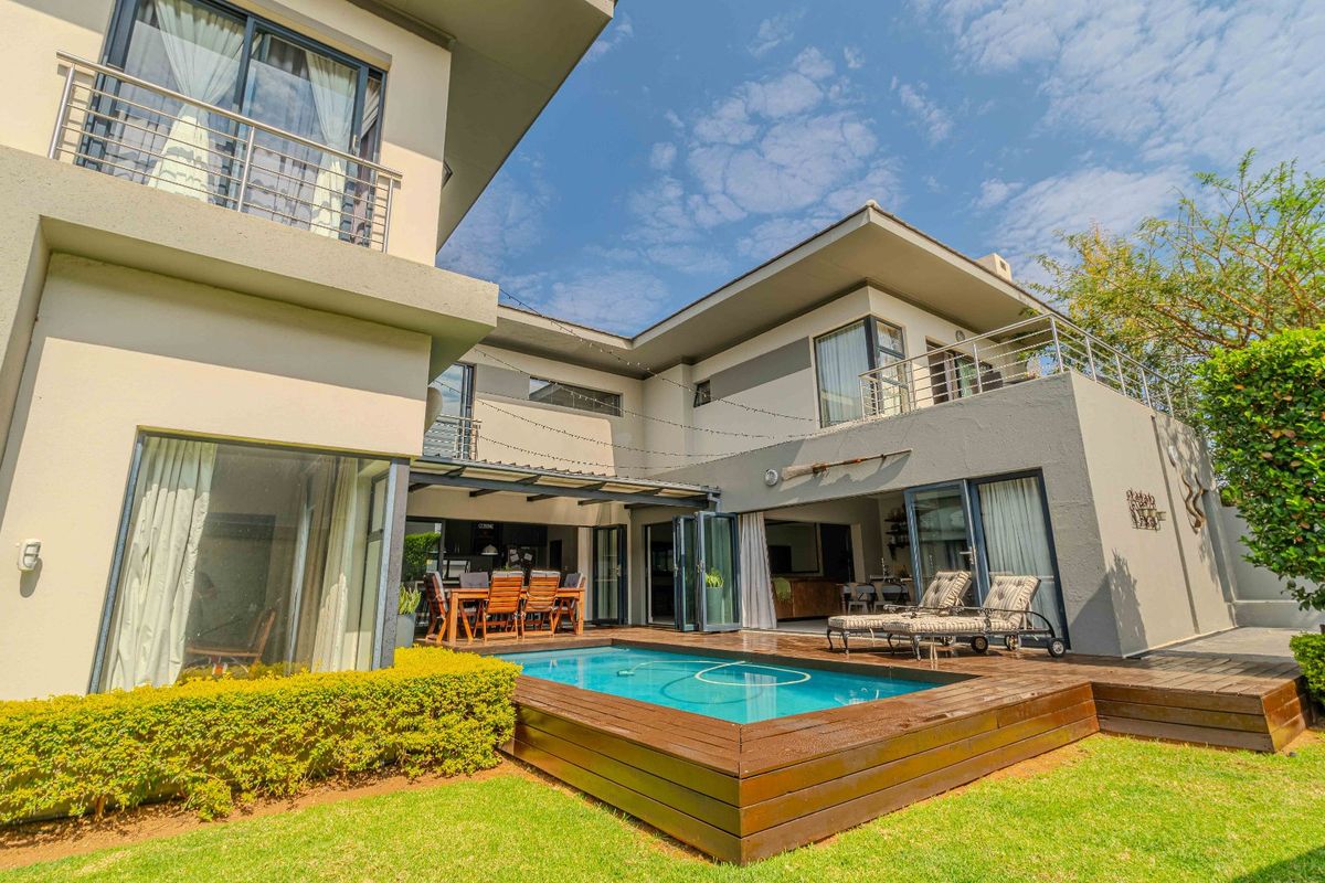 A modern double-story home featuring a swimming pool with timber decking, a covered patio area, and upper-level balconies.