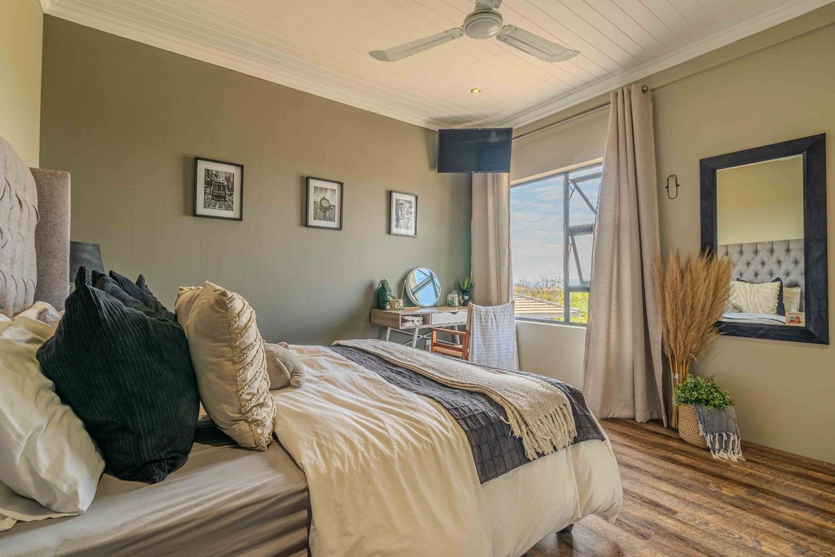 A well-maintained bedroom featuring wood-look flooring, a ceiling fan, and a large window providing natural light and exterior views.