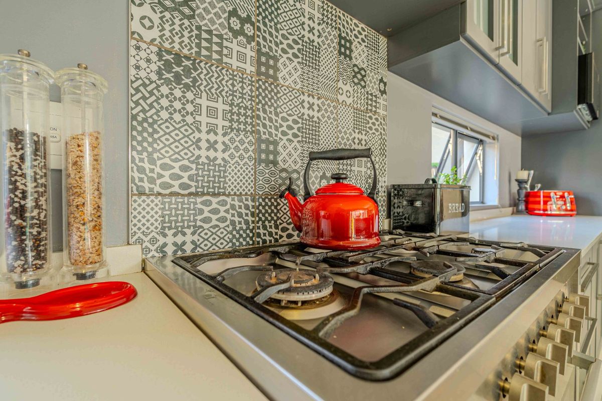 Close-up of a kitchen workspace featuring a built-in gas hob, patterned tile splashback, and stone-look countertops.