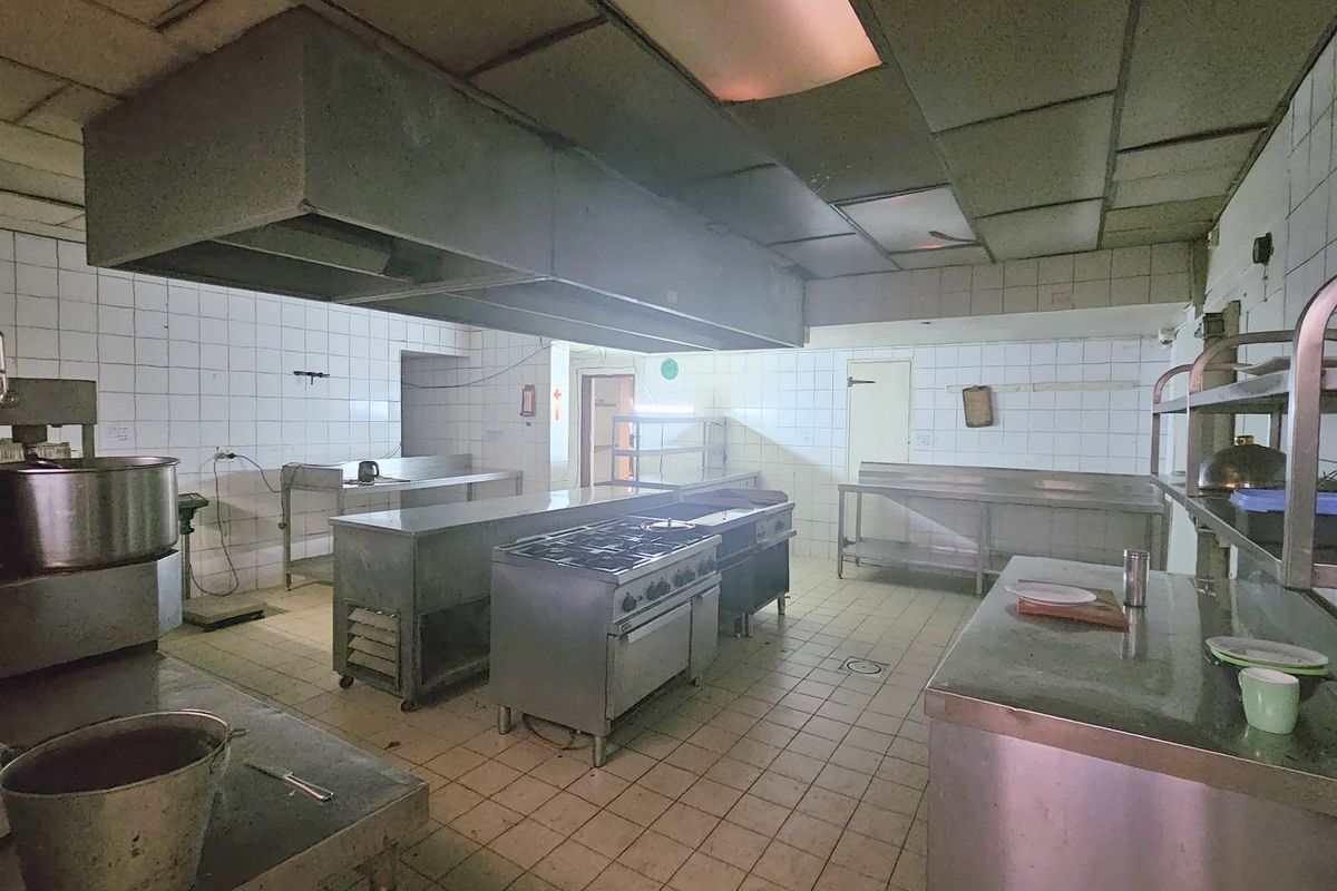 Commercial kitchen facility featuring stainless steel prep stations, a large extractor hood, gas range, and tiled finishes throughout.