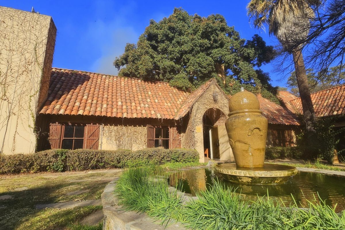 A charming commercial property exterior featuring a terracotta tiled roof, stone arched entrance, and a decorative stone fountain in the garden area.