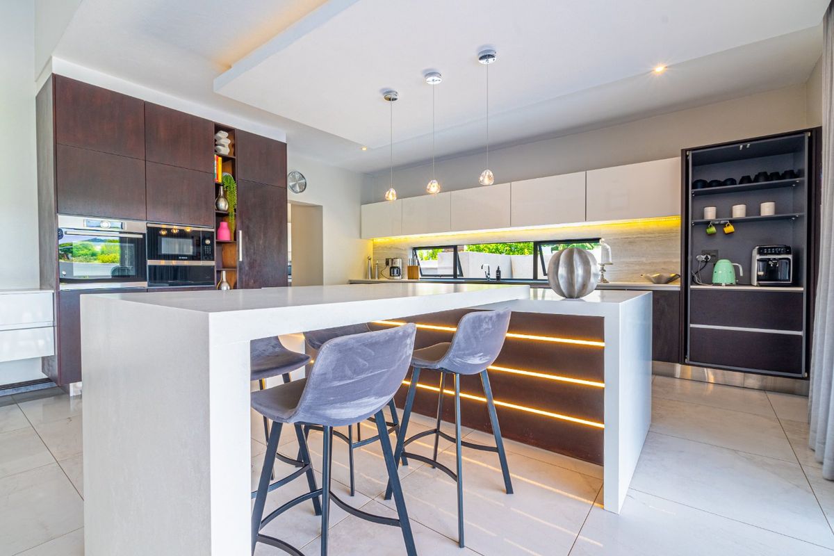 Modern kitchen featuring a large central island with breakfast bar seating, integrated cabinetry, built-in oven, microwave, and sleek under-cabinet LED lighting.