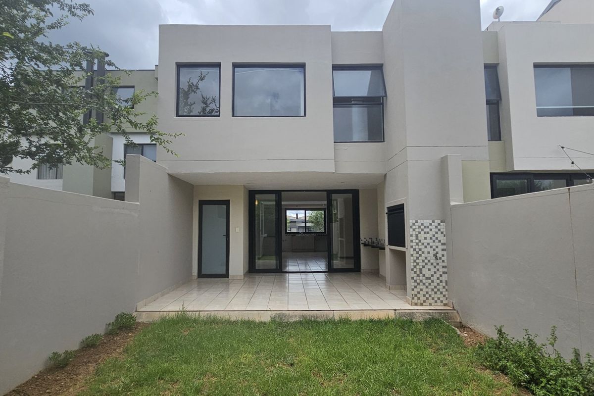 Rear view of a modern townhouse featuring a paved patio area with a built-in braai, leading into the open-plan living space.