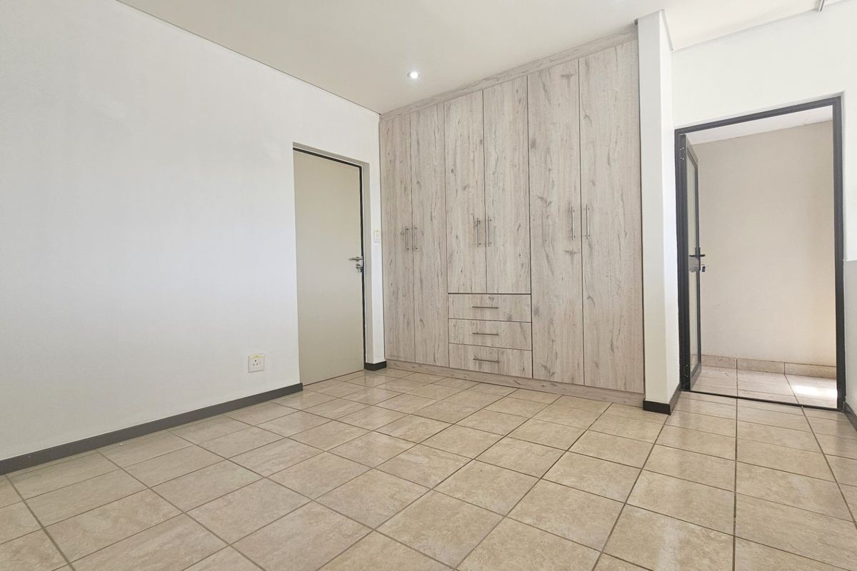 A bright, empty bedroom featuring neutral floor tiles and modern built-in wooden cabinetry with integrated drawers.