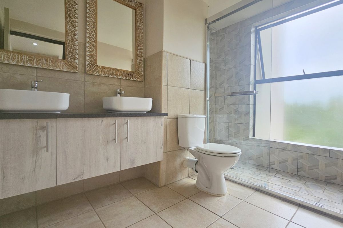Modern bathroom featuring a double vanity with stone countertop, a glass-enclosed walk-in shower, and neutral floor-to-ceiling tiling.