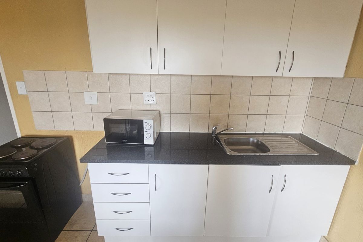 Compact kitchen featuring white cabinetry, dark laminate countertops, a stainless steel sink, tiled backsplash, and a freestanding stove.