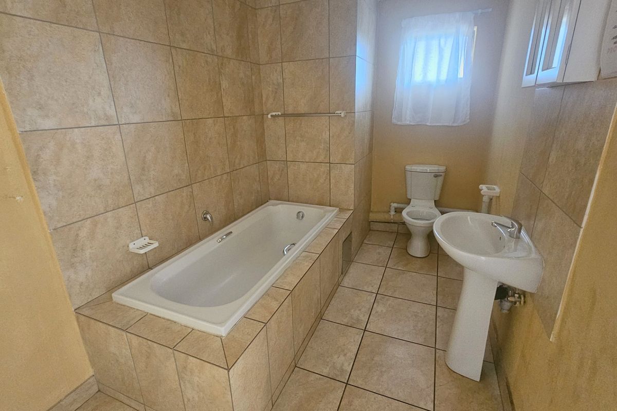 A functional bathroom featuring a built-in bathtub, pedestal sink, and toilet with neutral ceramic tiling throughout.