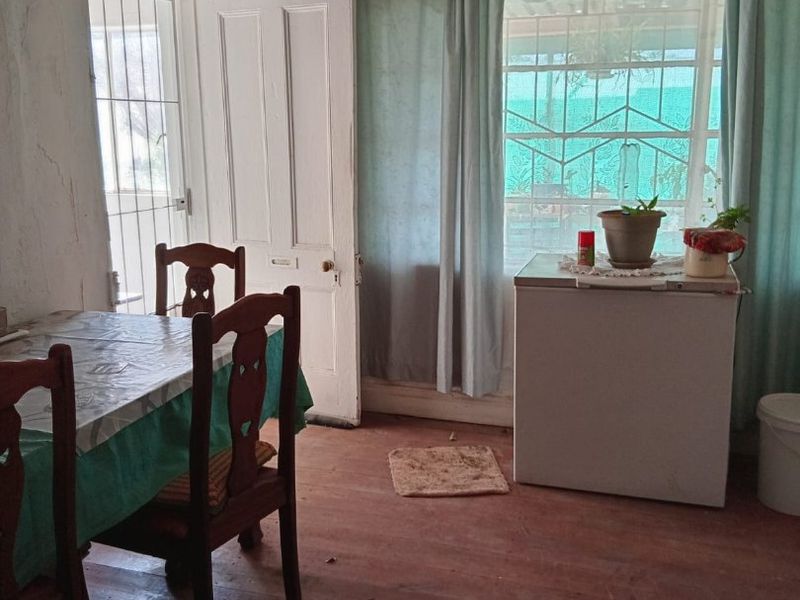 Dining area featuring original timber flooring, security gate access, and large windows with security bars, requiring cosmetic renovation and wall repairs.