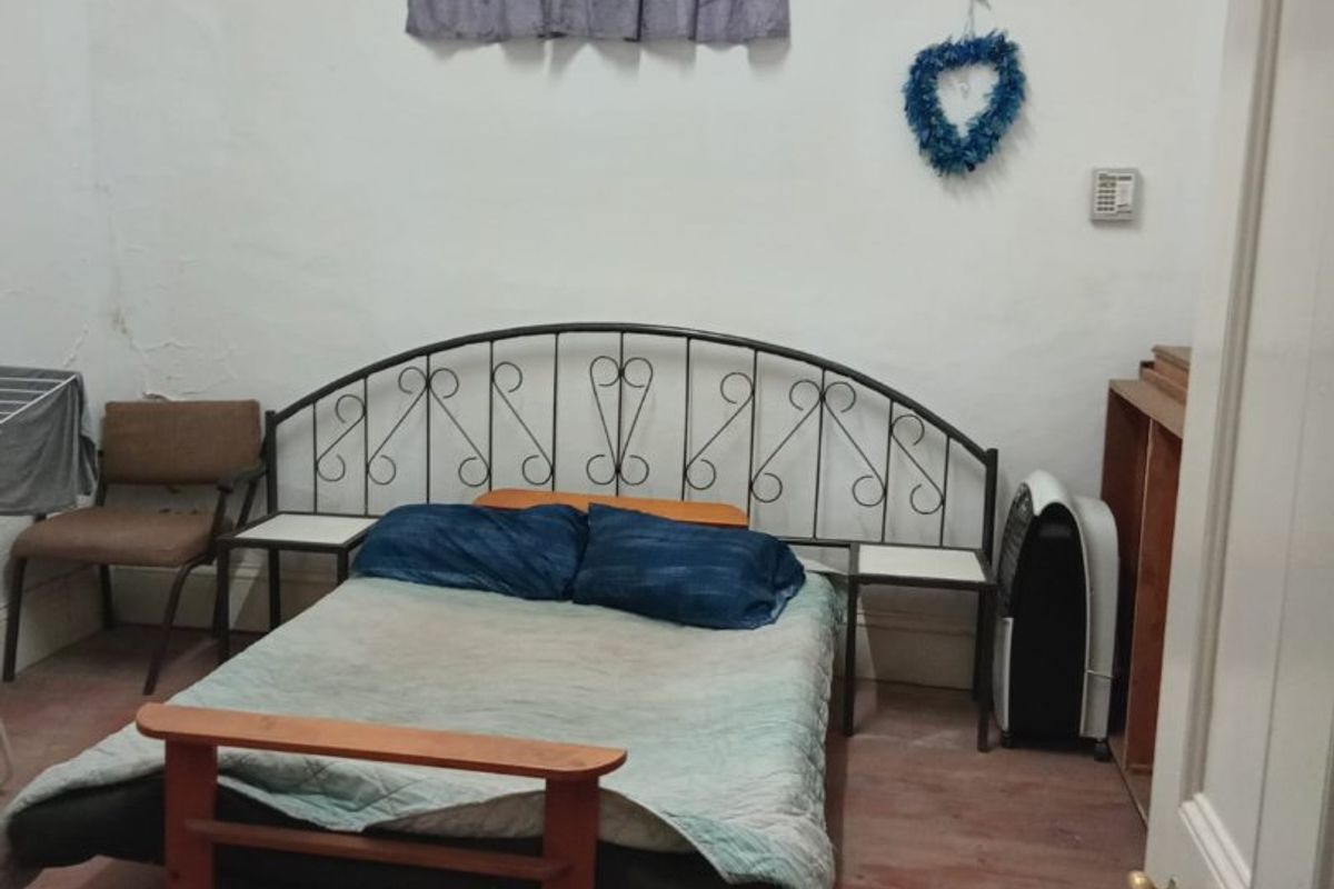 A bedroom featuring timber flooring and a window with security bars, showing signs of wear on the walls and floor.