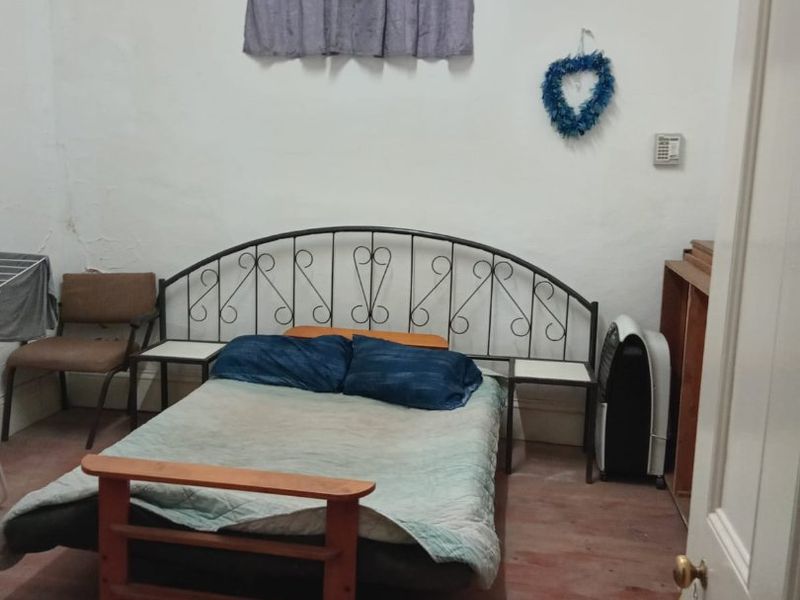 A bedroom featuring timber flooring and a window with security bars, showing signs of wear on the walls and floor.