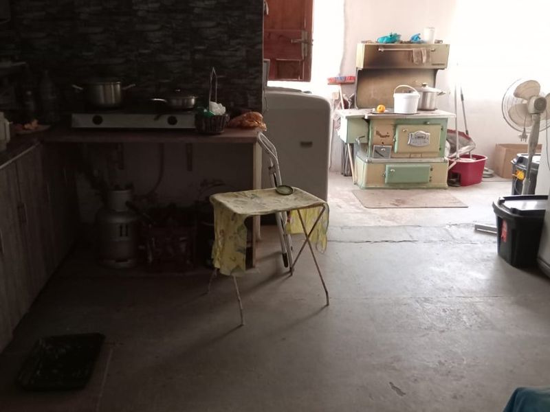 A rustic kitchen area featuring concrete flooring, stone-effect wall cladding, and a vintage wood-burning stove, requiring significant modernization and finish upgrades.