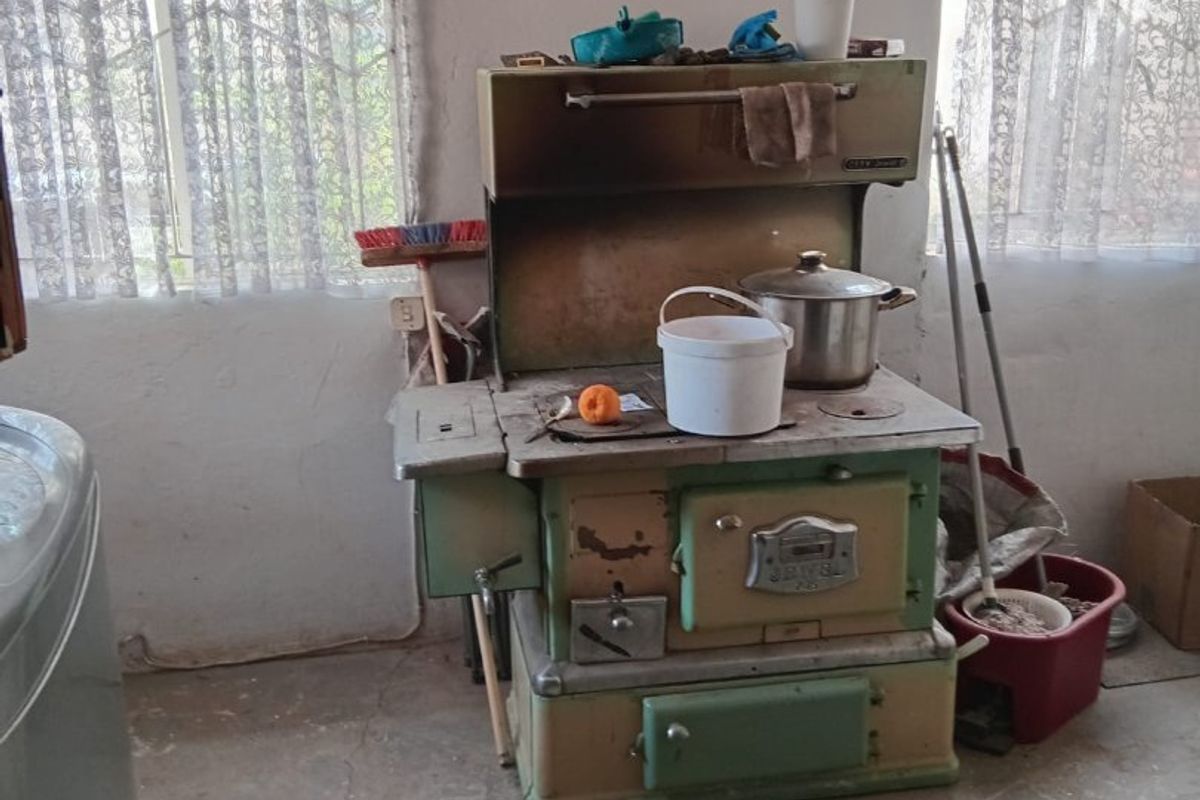A rustic kitchen area featuring a vintage wood-burning stove and exposed concrete flooring, requiring significant renovation and modernization of finishes.