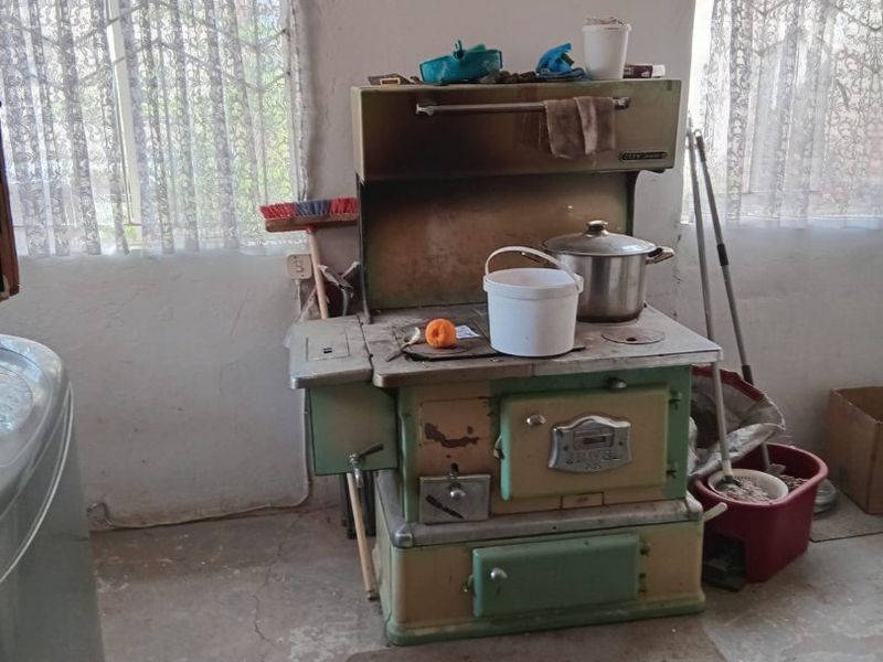 A rustic kitchen area featuring a vintage wood-burning stove and exposed concrete flooring, requiring significant renovation and modernization of finishes.