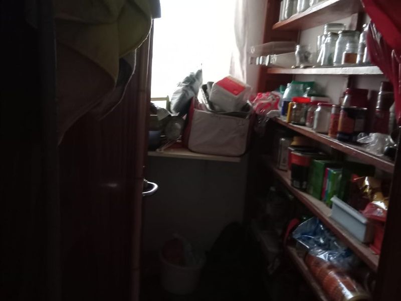 A small, narrow pantry or scullery area featuring built-in wooden shelving for storage.