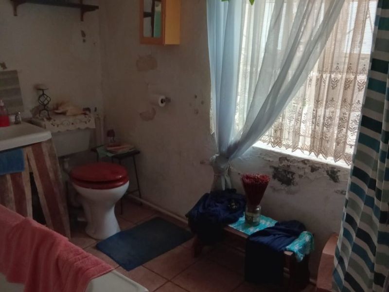 A bathroom featuring a bathtub, pedestal sink, and toilet, currently requiring significant wall repairs and cosmetic renovation to restore its condition.