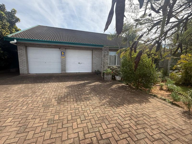 Front exterior view of the property featuring a double garage with roller doors, paved driveway, and established garden landscaping.