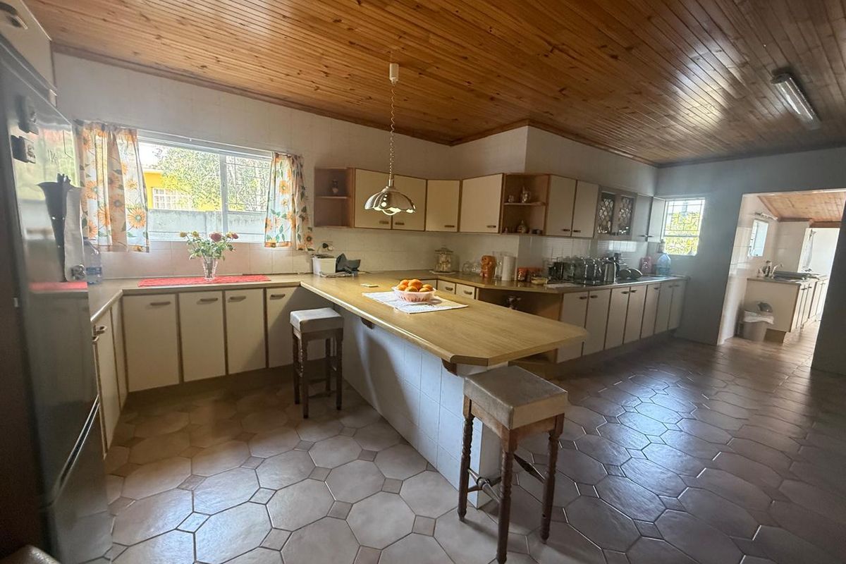 Spacious kitchen featuring extensive cabinetry, a central breakfast bar, tiled flooring, and a timber-paneled ceiling, offering a functional layout with potential for modernization.