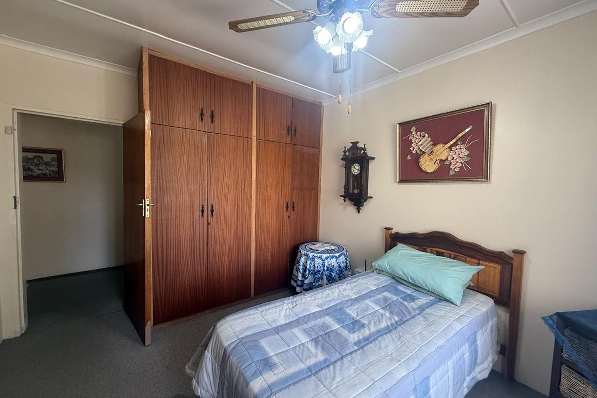 A bedroom featuring built-in wooden cupboards, a ceiling fan with integrated lighting, and neutral wall finishes.