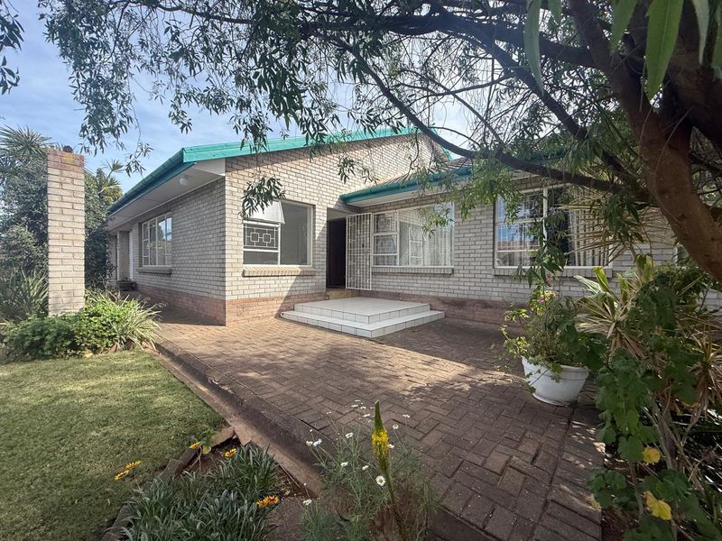 A single-story brick house featuring a paved front patio, tiled entrance steps, and established garden surroundings.