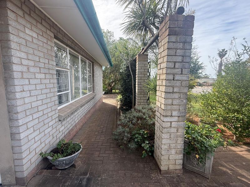 A side exterior view of the house featuring a paved walkway, brick facade, and decorative brick pillars leading into the garden area.