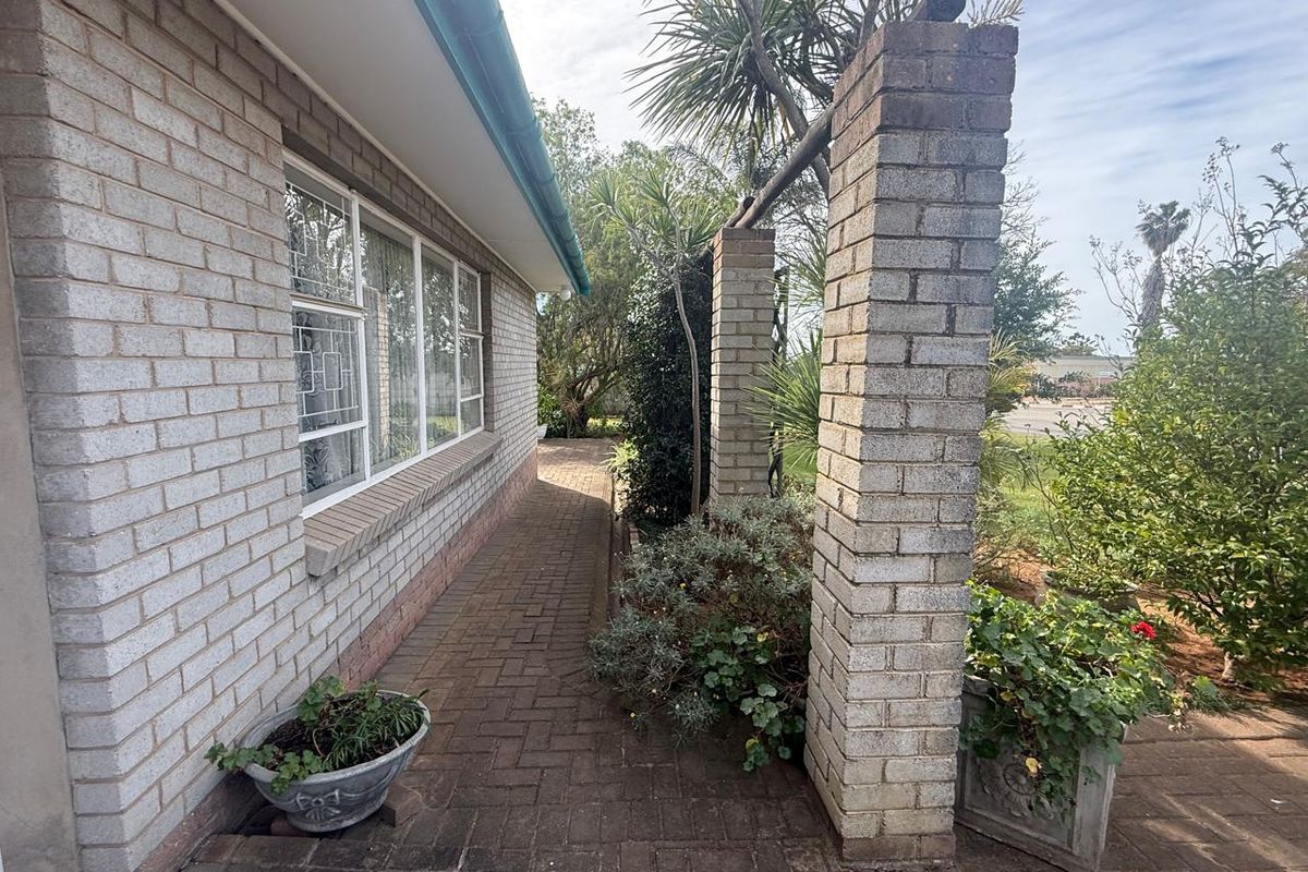 A side exterior view of the house featuring a paved walkway, brick facade, and decorative brick pillars leading into the garden area.