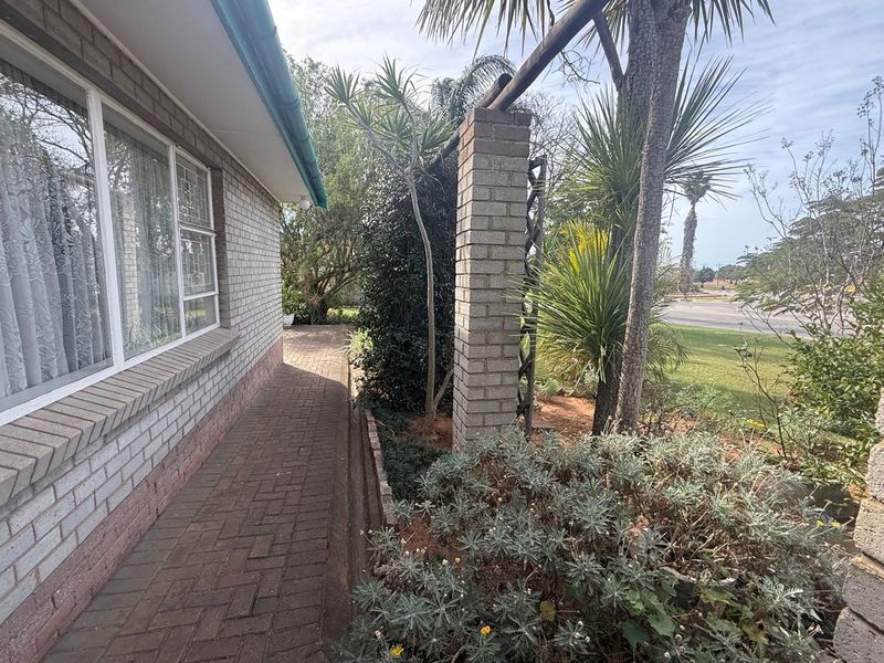 A side exterior view of the house featuring a brick facade, paved walkway, and established garden landscaping.