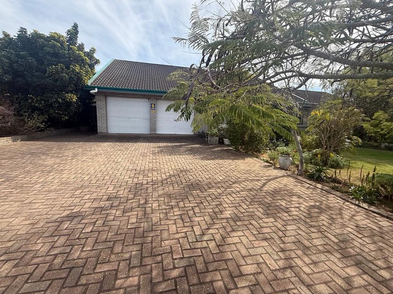 A paved driveway leading to a double garage with white roller doors, set within a landscaped garden area.
