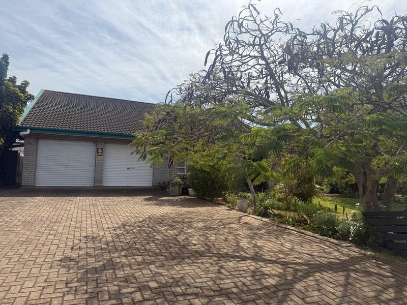Front exterior view of the property featuring a paved driveway, double garage with roller doors, and established garden landscaping.