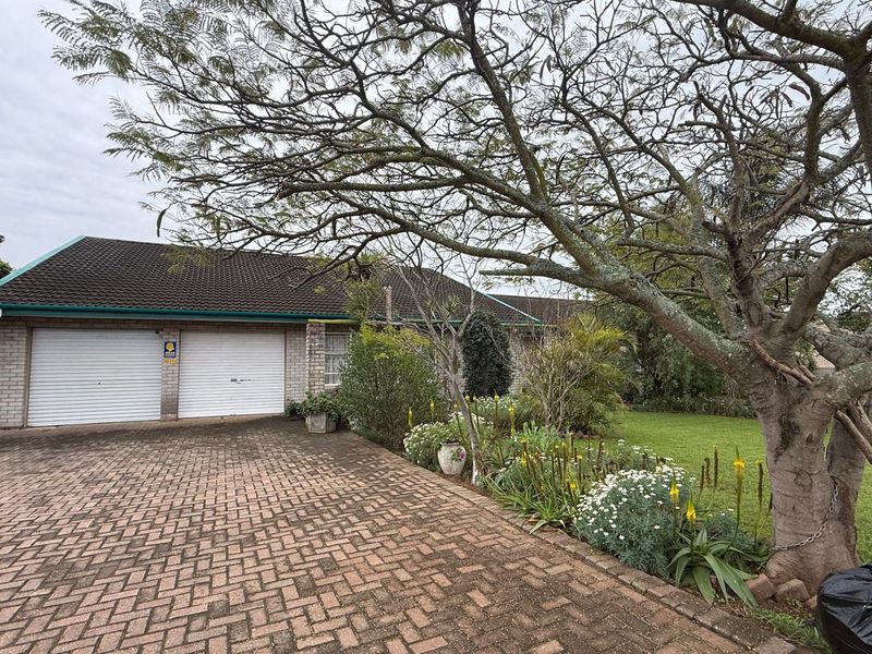 Front exterior view of the property featuring a double garage, paved driveway, and established garden with mature trees.