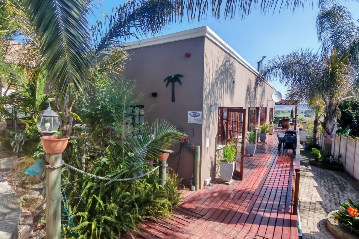 Rear exterior view featuring a timber deck, paved pathways, and multiple french door access points to the main dwelling.