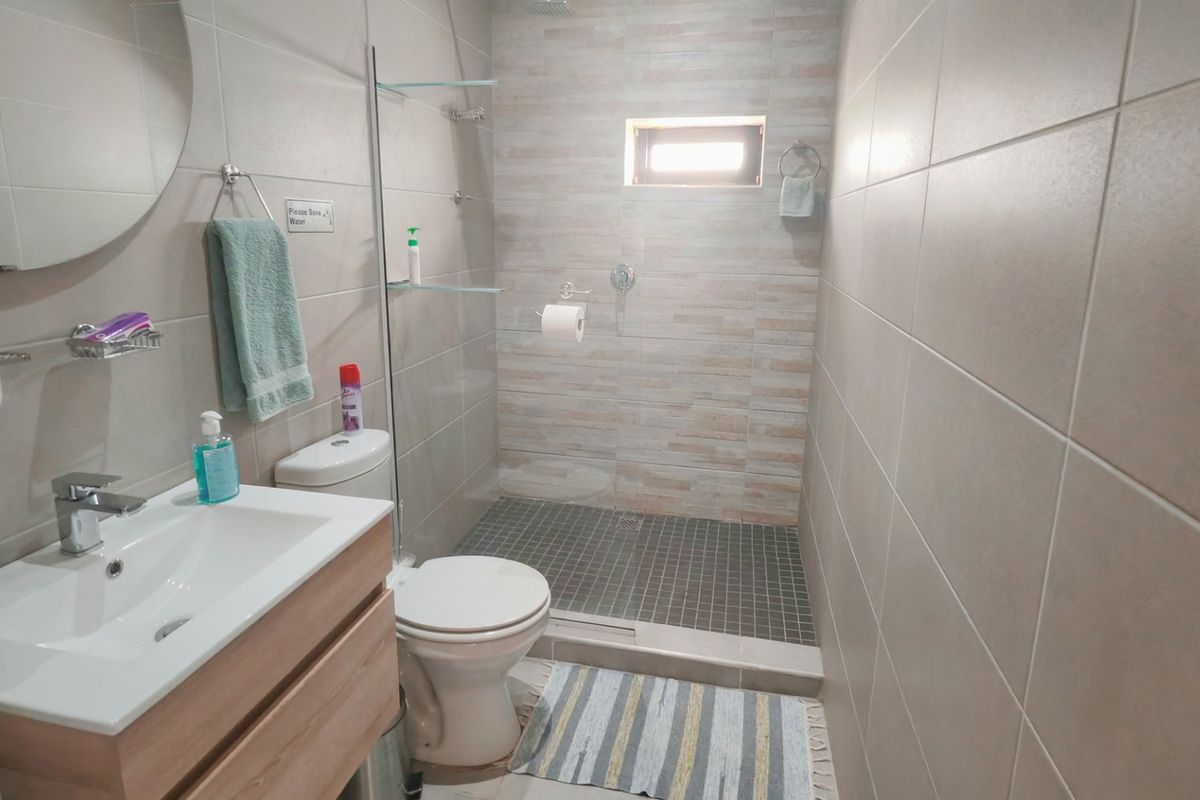 Modern bathroom featuring a vanity cabinet with basin, a walk-in shower with glass screen, and neutral wall and floor tiling.