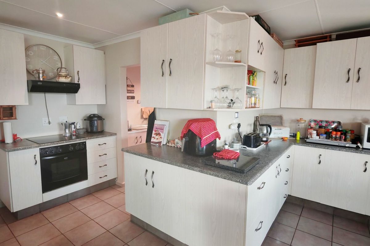 Functional kitchen featuring light-toned built-in cabinetry, laminate countertops, integrated oven and hob, and tiled flooring with a connected scullery area.