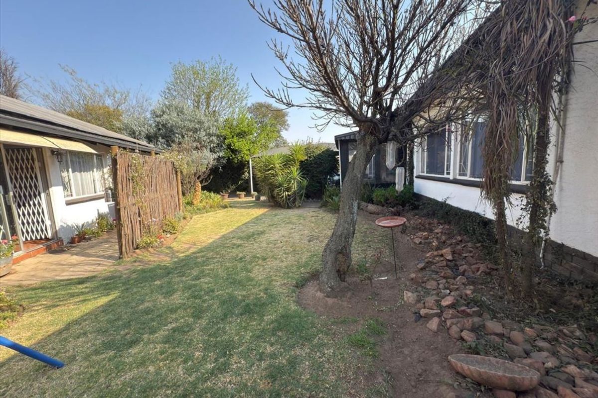 A private rear garden area featuring a lawn, mature trees, and a paved patio section adjacent to the main house structure.